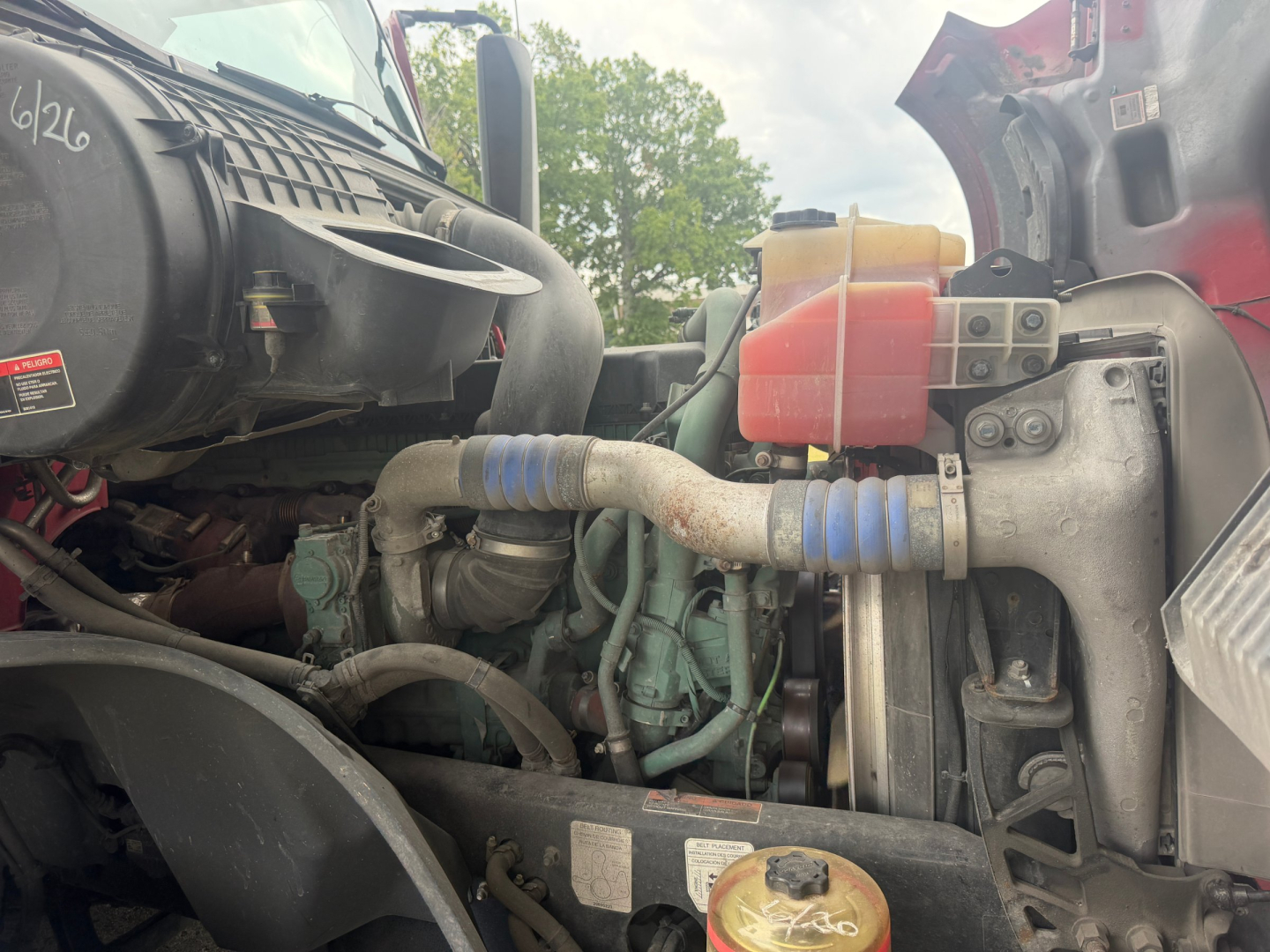 Volvo VNL64T760 engine bay view showing coolant reservoir and hoses with blue clamps, air intake, and surrounding components.