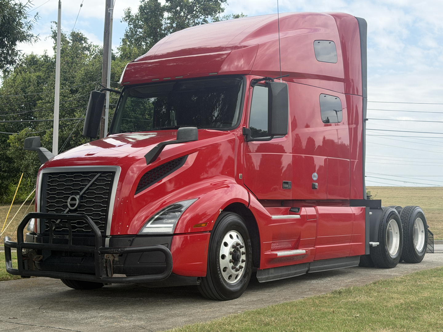 Volvo VNL64T760 tractor in red paint view from front-left showing grille guard, aerodynamic headlights, stacked sleeper cab, and dual rear axles.