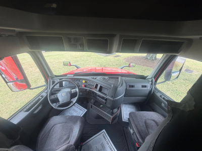 Interior of Volvo VNL truck cab showing steering wheel, dashboard, and driver's seat with center console and overhead storage panel.