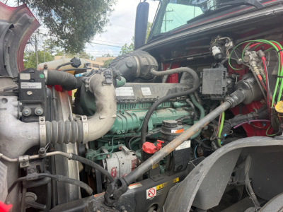 Volvo VNL64T760 truck engine bay viewed from passenger side showing green engine block, various hoses, and battery wiring.
