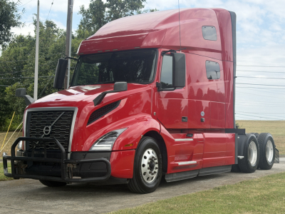 Volvo VNL64T760 tractor in red paint view from front-left showing grille guard, aerodynamic headlights, stacked sleeper cab, and dual rear axles.