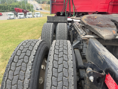 Volvo VNL64T760 truck chassis with dual rear axles and treaded tires; visible label on red underride guard with small text; background shows service yard.