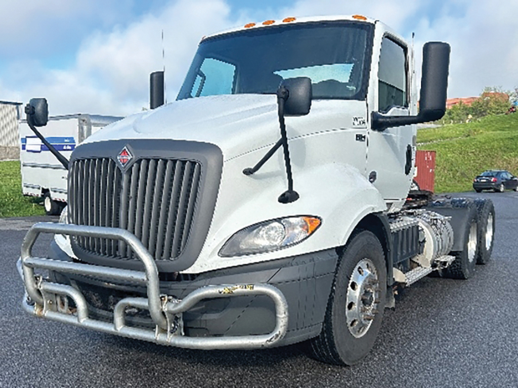 Truck shows 2019 International RH613 conventional daycab with front grille guard and dual rear axles, white cab, large side mirrors, VIN plate not visible.