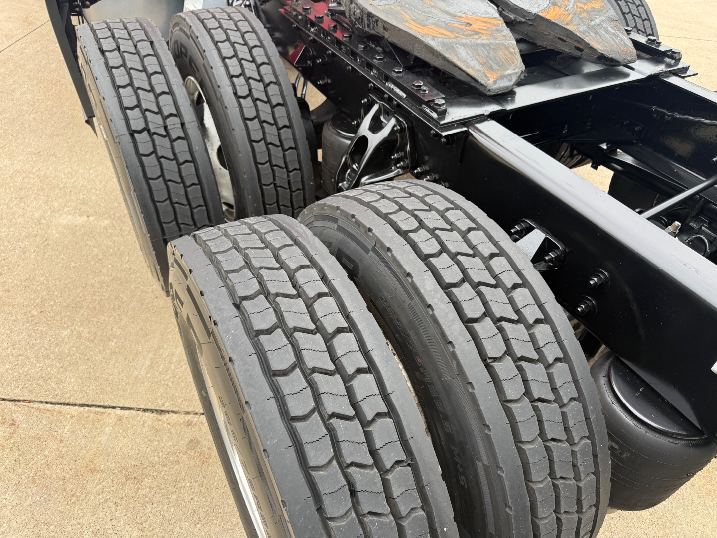 Kenworth truck chassis showing dual rear axles with treaded tires and undercarriage components.