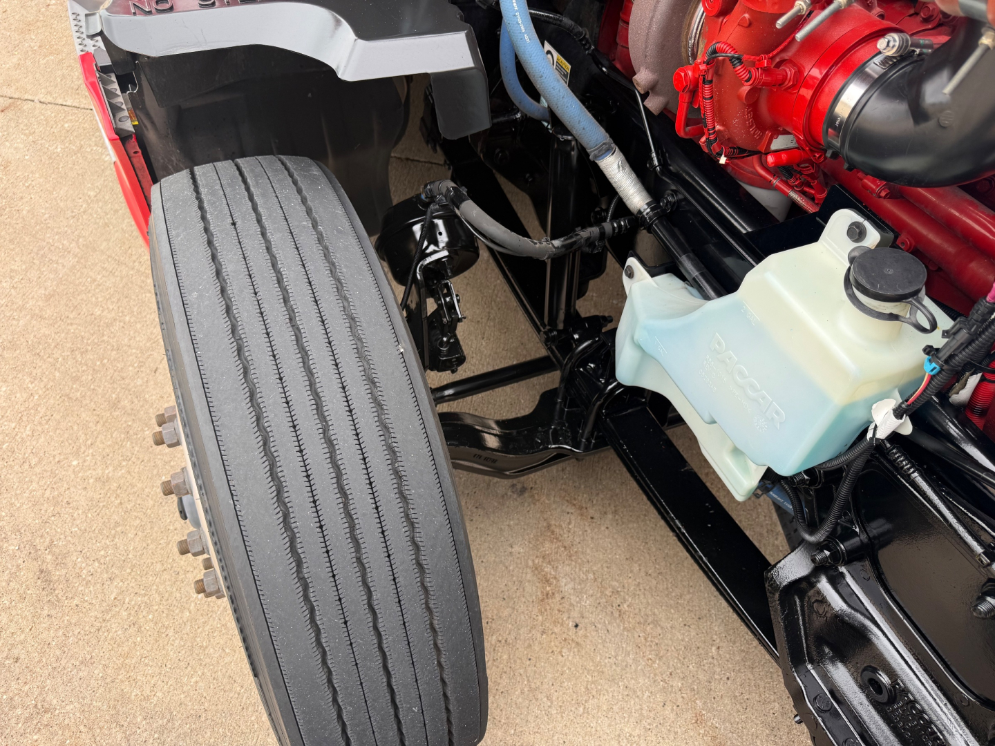 Kenworth T680 front engine bay with tire and coolant reservoir; visible labels include no legible serials in this view.