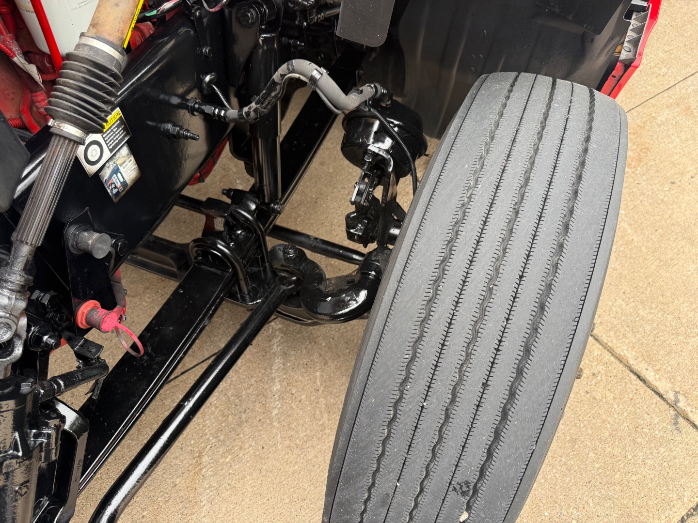 Truck front suspension and steering components visible in the engine bay area of a 2023 Kenworth T680, with a large front tire on the right.
