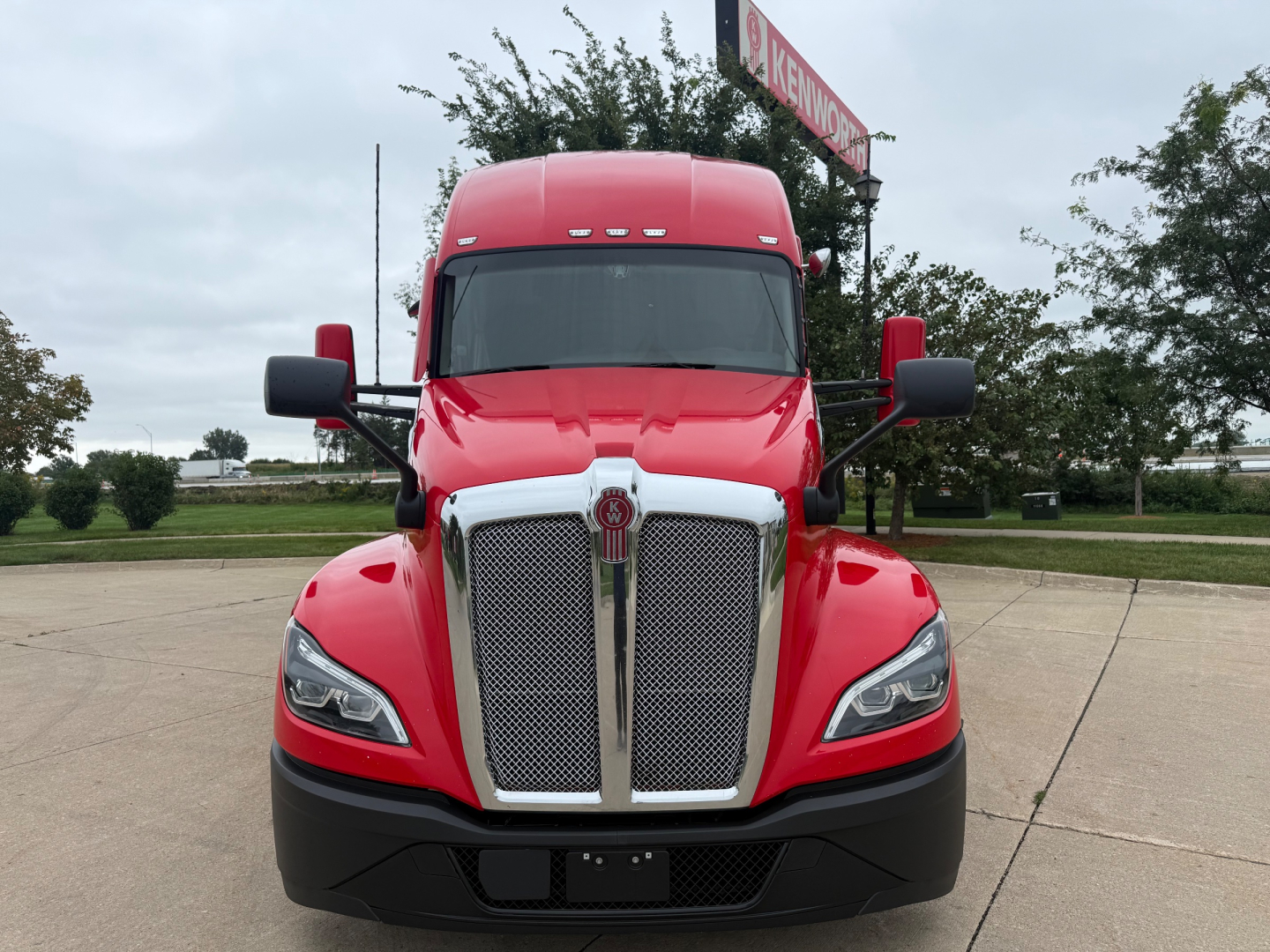 Kenworth T680 tractor front view showing chrome grille and red cab with black bumper.
