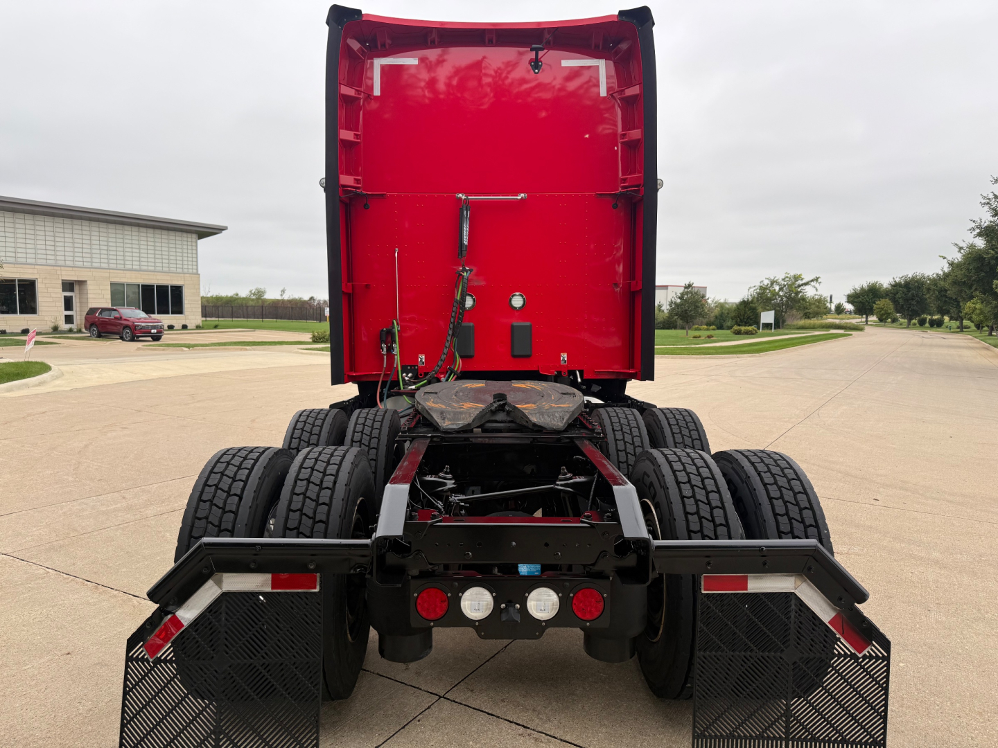 Back view of a red Kenworth T680 tractor with dual rear axles and mud flaps, showing the chassis and rear lights, no cab attached.