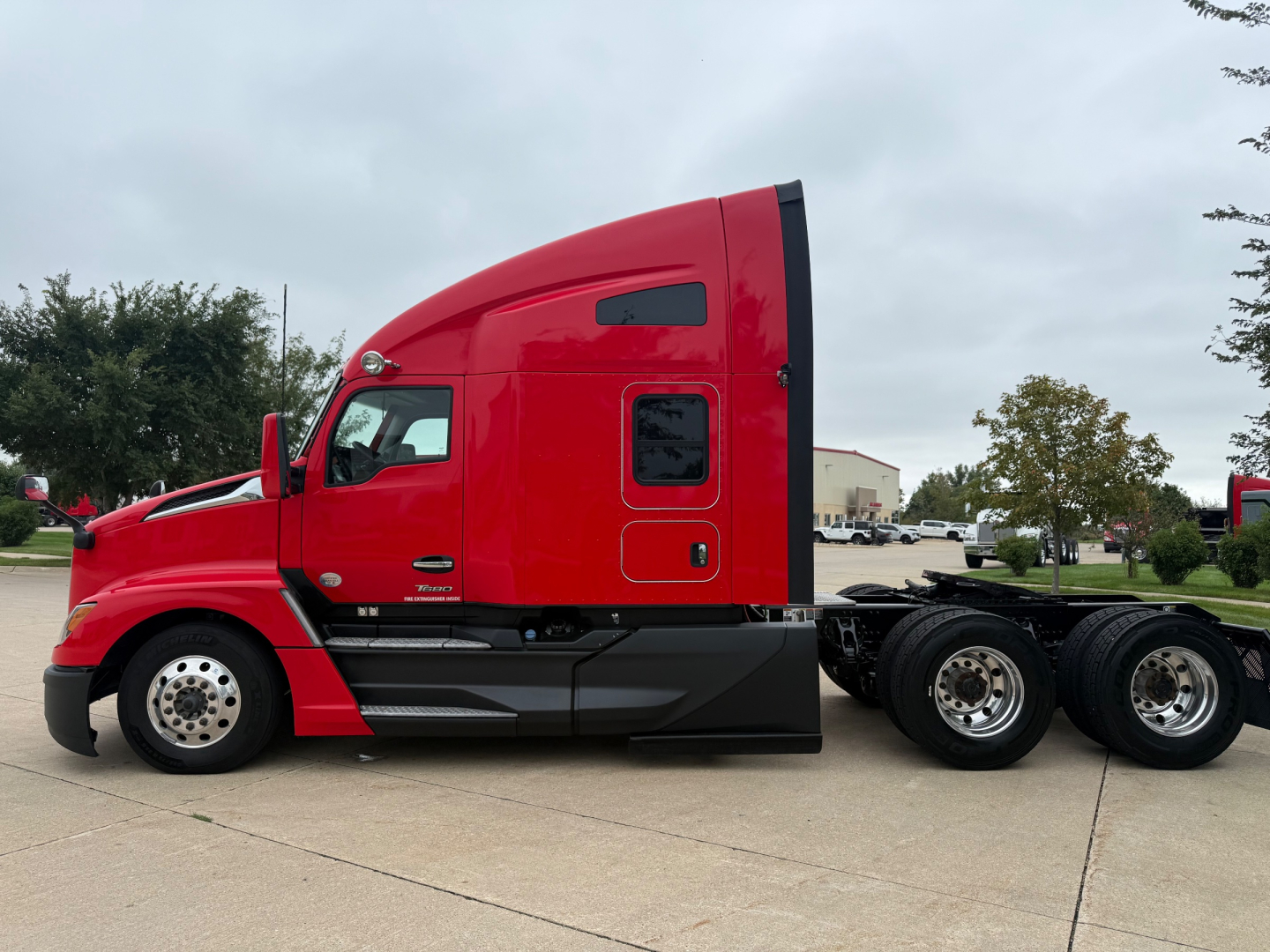 Kenworth T680 sleeper tractor in red, side view showing cab and chassis with dual rear axles.
