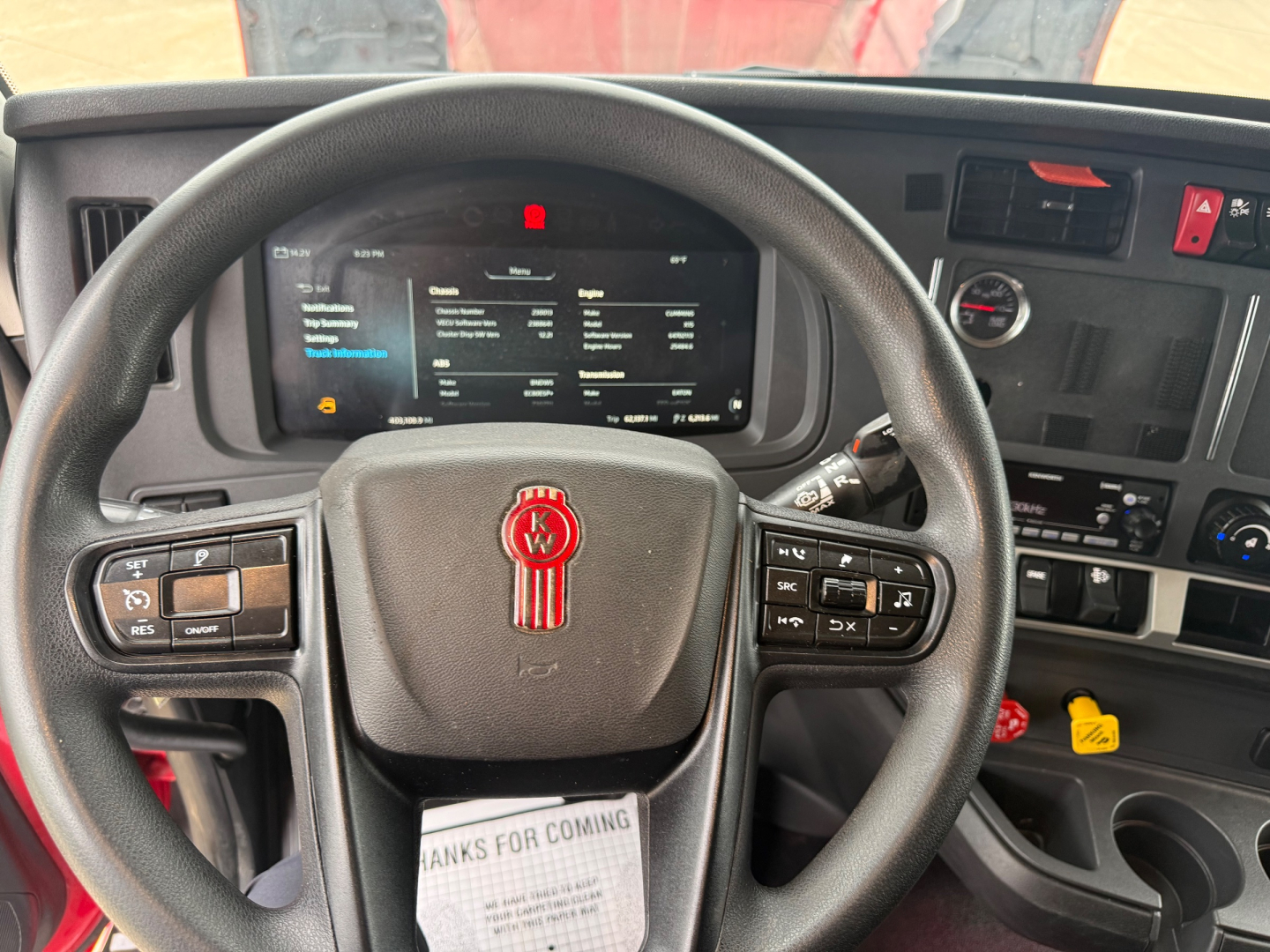 Kenworth truck interior steering wheel with dashboard display and controls; visible text on screen and buttons.