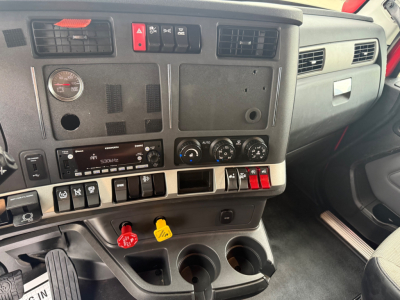 Kenworth T680 dash area showing control panel, gauges, and switches; two cup holders and yellow/red hazard levers visible.