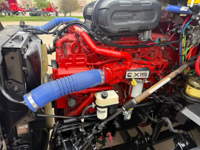 Kenworth T680 engine bay showing RED PACCAR engine with blue intake hoses, air filter housing, coolant reservoir, and various hoses and wiring.