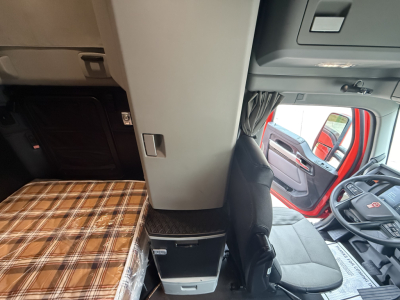 Interior of a Kenworth truck cab with a plaid bunk, driver seat, and dashboard visible. Text: none readable on image itself.