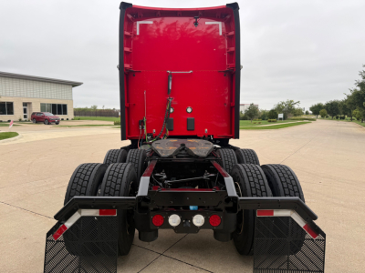 Back view of a red Kenworth T680 tractor with dual rear axles and mud flaps, showing the chassis and rear lights, no cab attached.