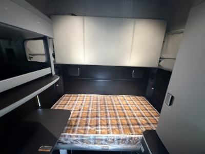 Kenworth T680 sleeper cab interior showing bunk bed with plaid mattress and side storage compartments.