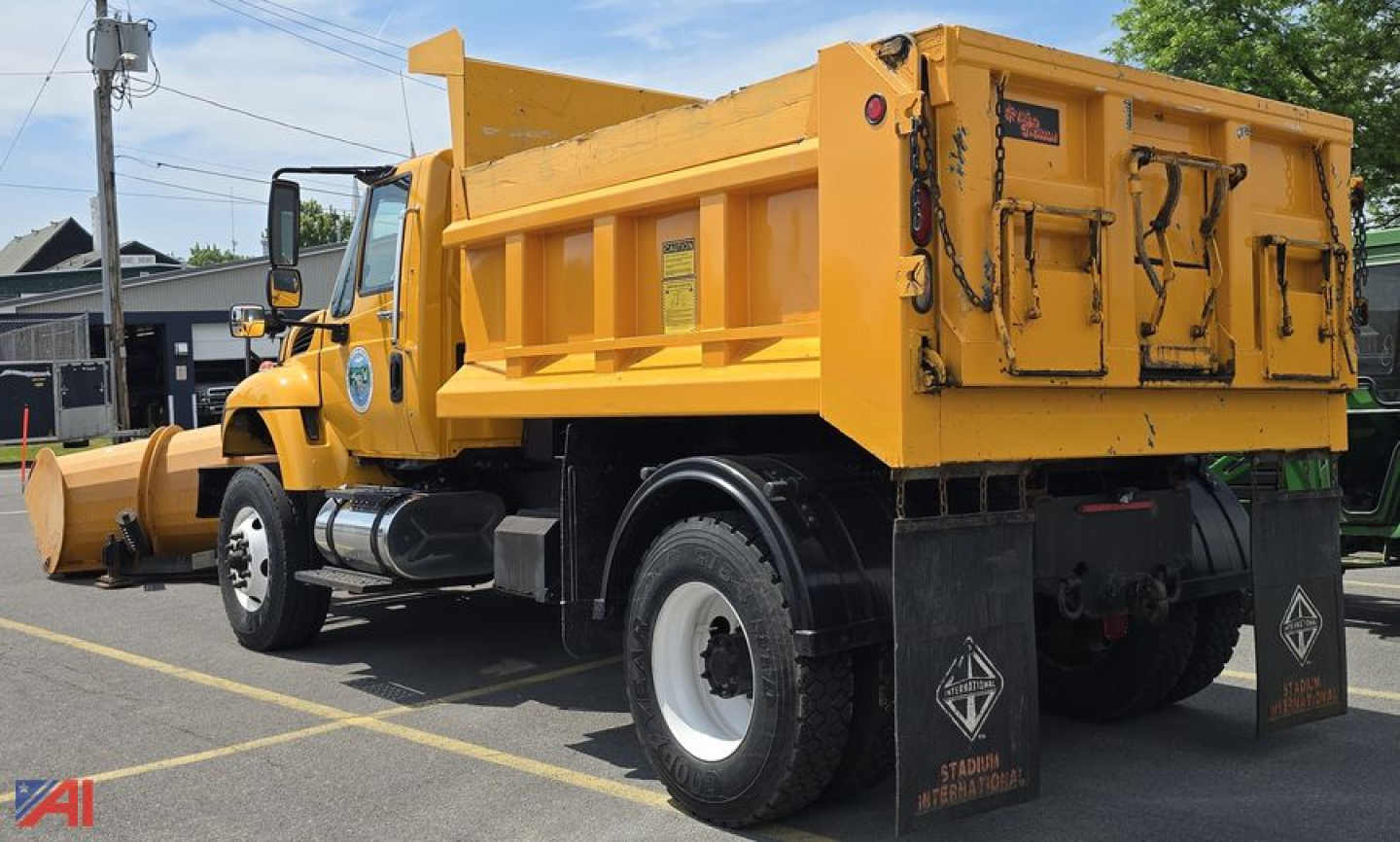 Dump truck side rear view showing yellow International WorkStar 7500 with plow attachment and dump bed in parked lot.
