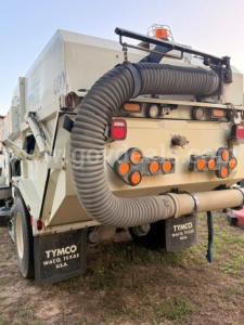 Dump truck rear showing large flexible vacuum hose and multiple circular ports; taillights and mud flaps; TYMO mud flaps in Waco, Texas; orange beacon on top.