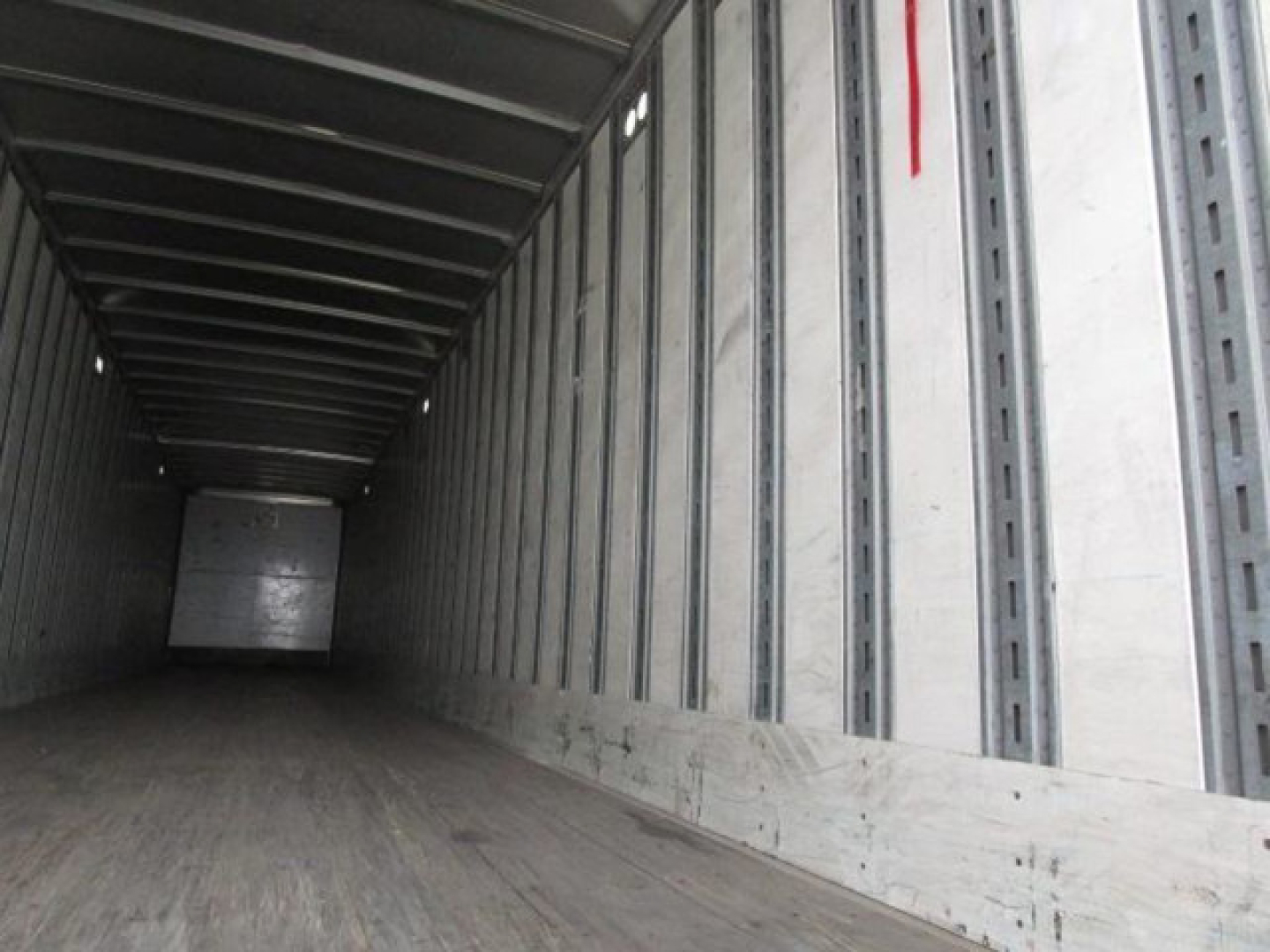 Trailer interior showing long empty box with wooden floor and metal side walls; rear door closed.