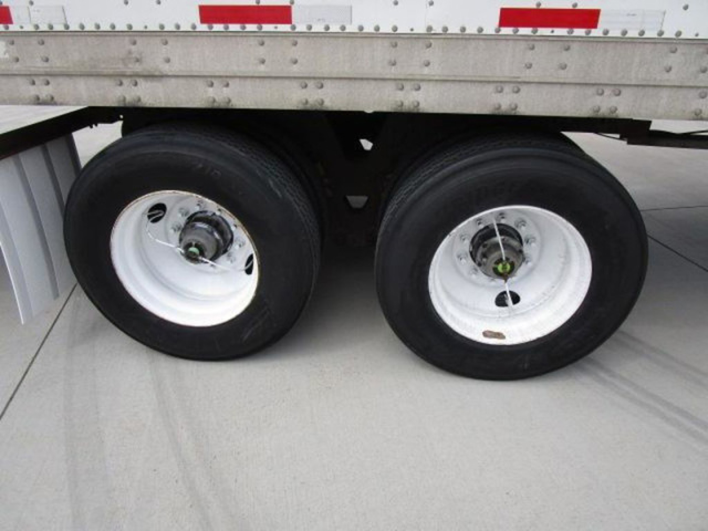 Two trailer wheels under a Stoughton van trailer, shows dual rear axles with white rims and black tires, undercarriage and side of trailer with aluminum side panels.