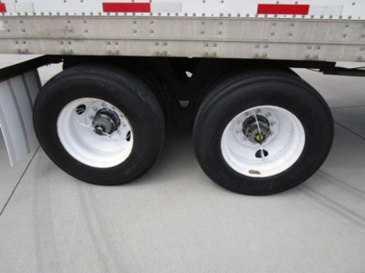 Two trailer wheels under a Stoughton van trailer, shows dual rear axles with white rims and black tires, undercarriage and side of trailer with aluminum side panels.
