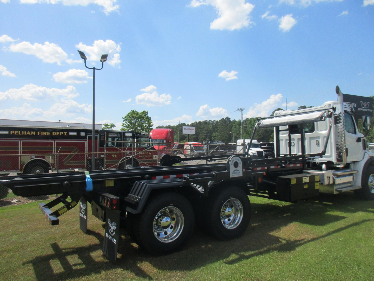 Western Star 47X truck with roll-off chassis showing dual rear axles and chrome wheels, flatbed hooklift frame in foreground, white cab in background.