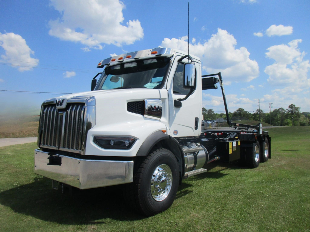 Truck with chrome grille and dual rear axles in a grassy lot, 2026 Western Star 47X roll-off configuration, VIN 3BJHBPFM1TDWW2259.