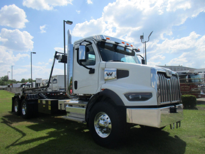 White Western Star 47X roll-off truck in profile view showing cab with chrome grille, side mirrors, and flatbed with hydraulic equipment.