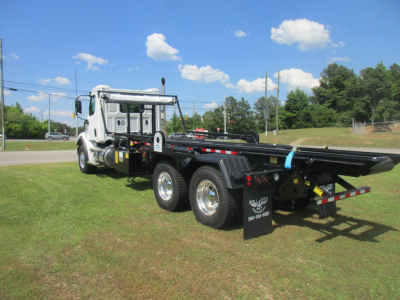 Western Star 47X truck chassis with roll-off bed and white cab, showing dual rear axles and black bed with safety reflectors.