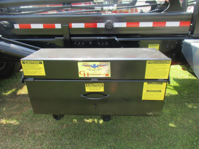 Western Star 47X rolloff truck side view showing a black toolbox with yellow caution labels and a central handle mounted under a reflective strip