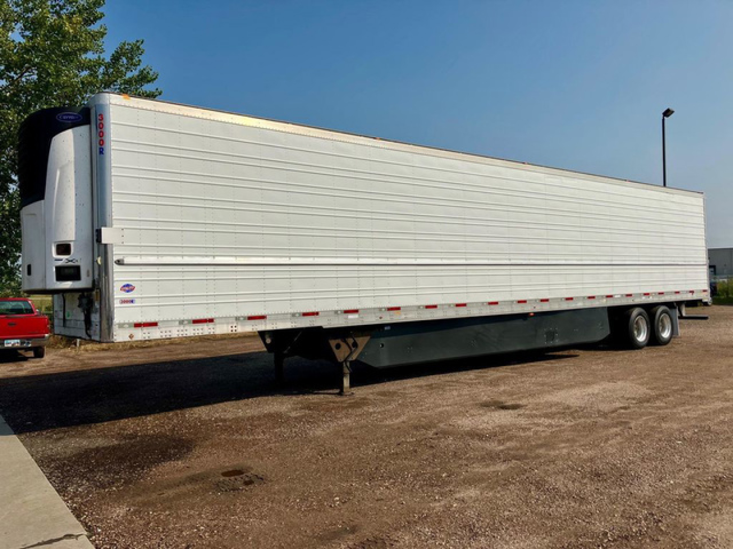 Utility reefer trailer side view showing refrigerated trailer with white aluminum panels and two axles, landing gear, and front refrigeration unit.