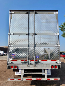 Utility reefer trailer rear view showing double doors with diamond plate quad hinges and latches, red rear lights, bumper, and reflective tape.