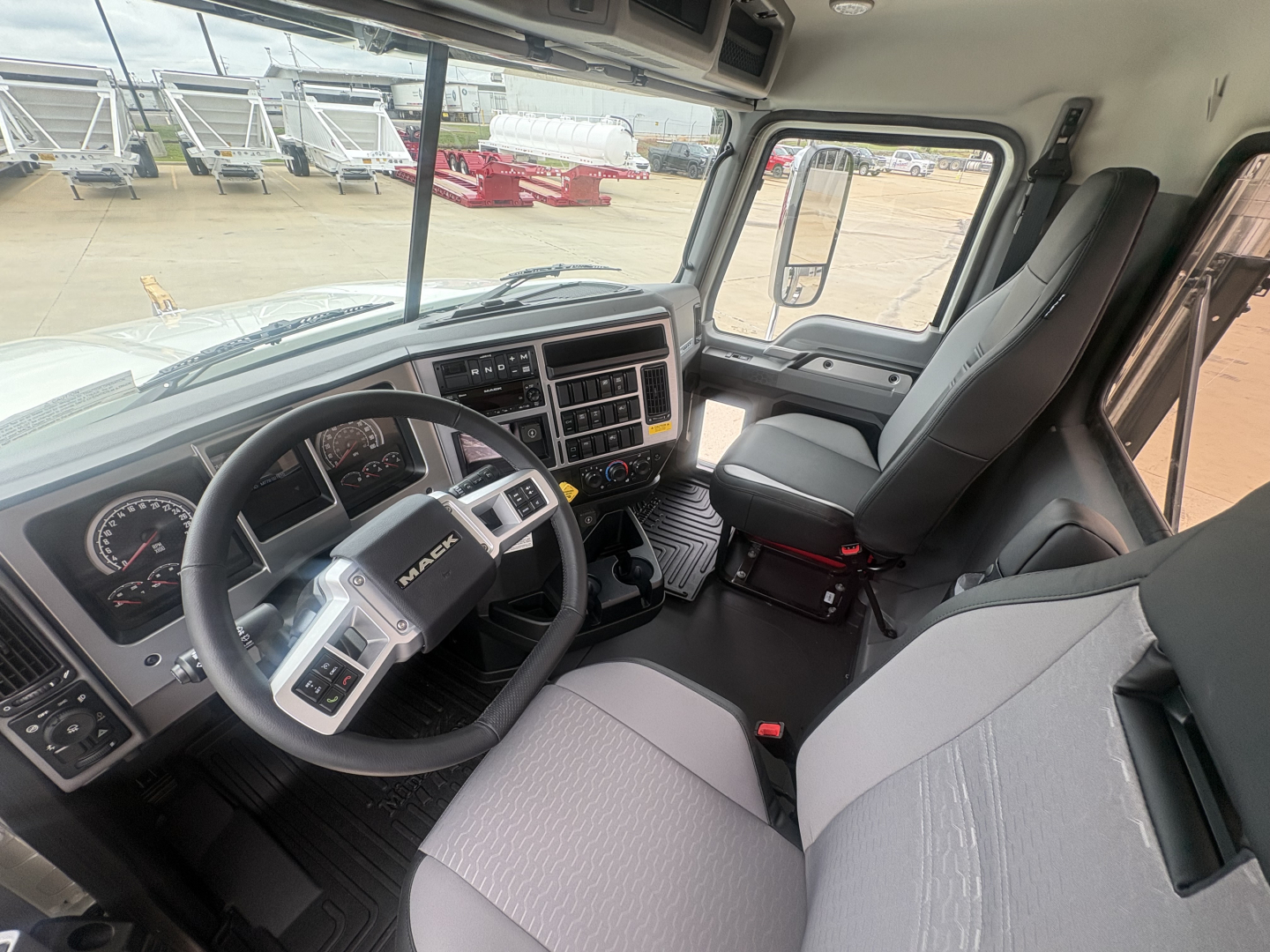Cab interior of a Mack PI64T truck showing steering wheel, dashboard, and right-side passenger seat.