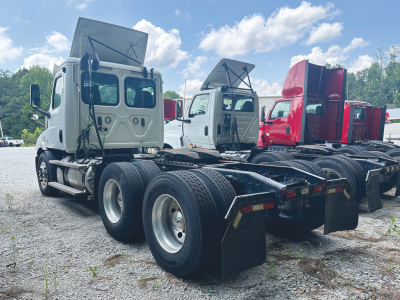 Freightliner Cascadia 116 truck cab and chassis with raised hood open, rear dual-axle configuration, two other cabs in background.