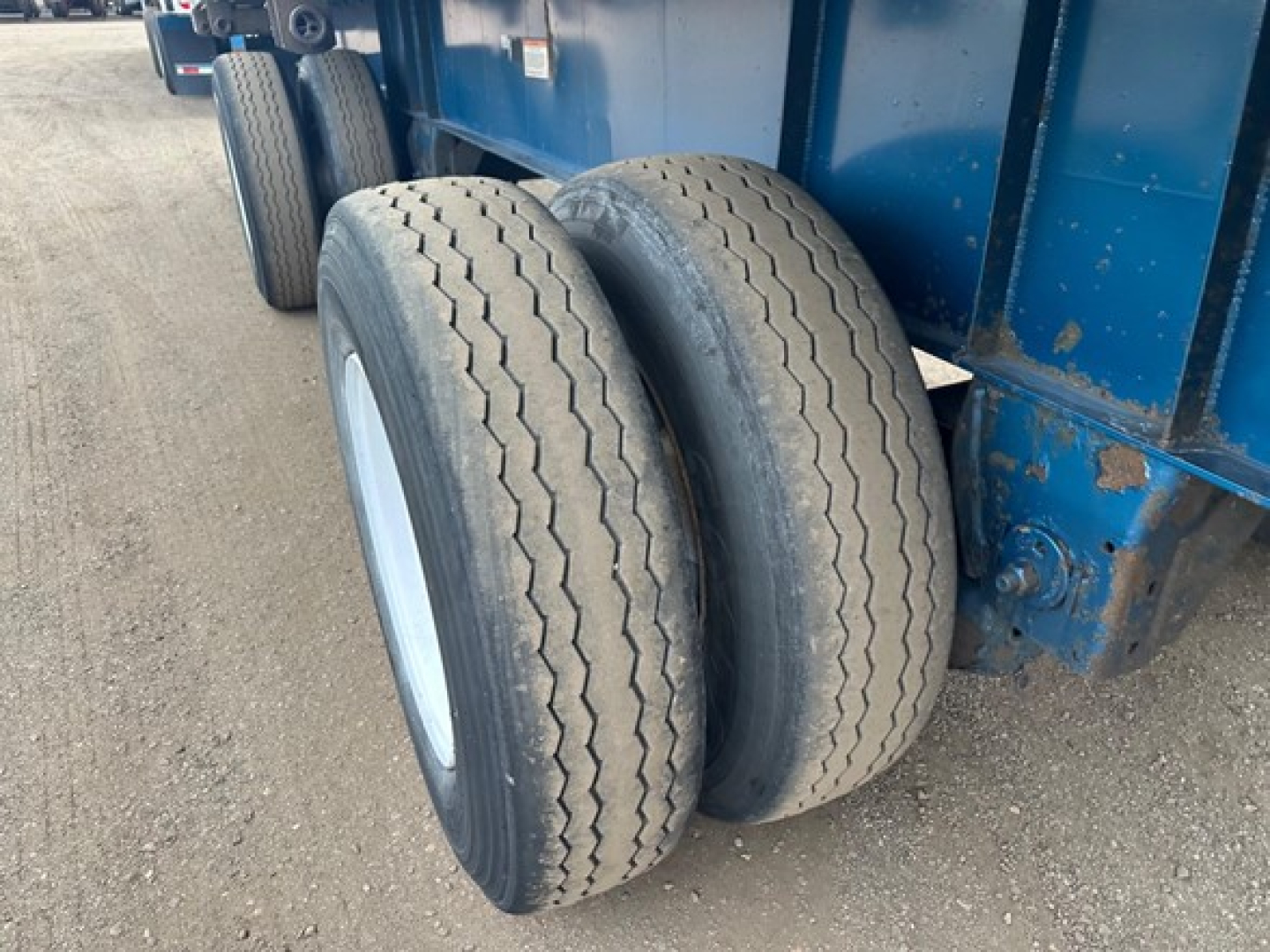 Flatbed trailer dual tires and blue frame showing treaded tires and wheel hubs.