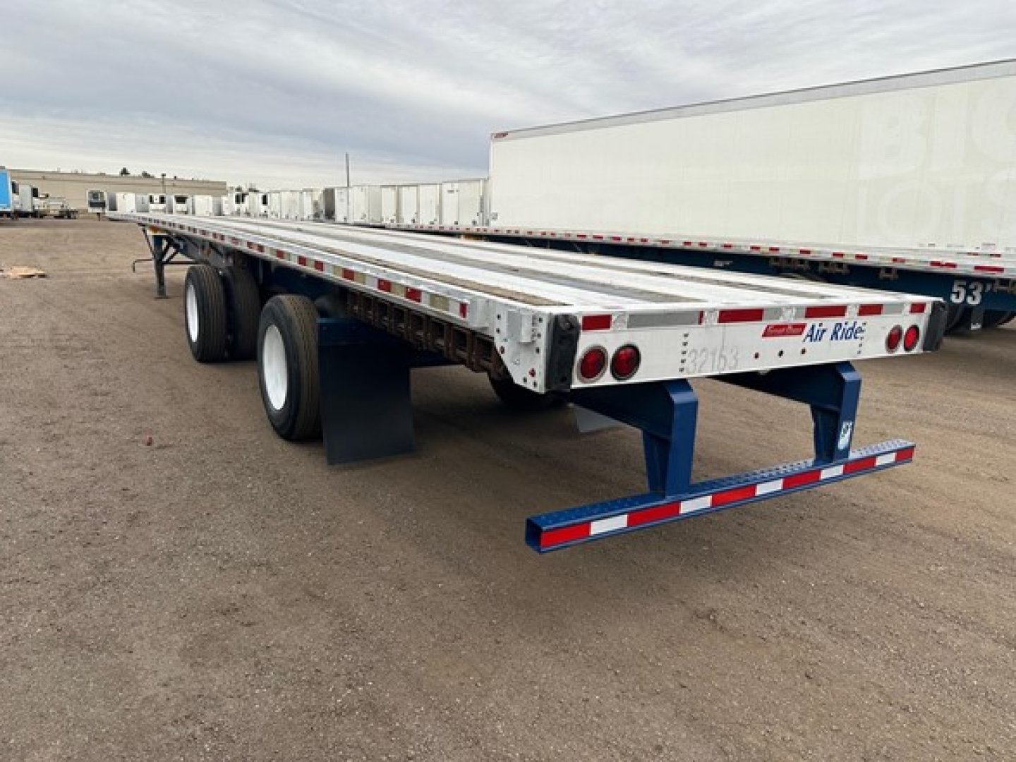 Flatbed trailer with dual rear axles showing long aluminum deck and safety rails.