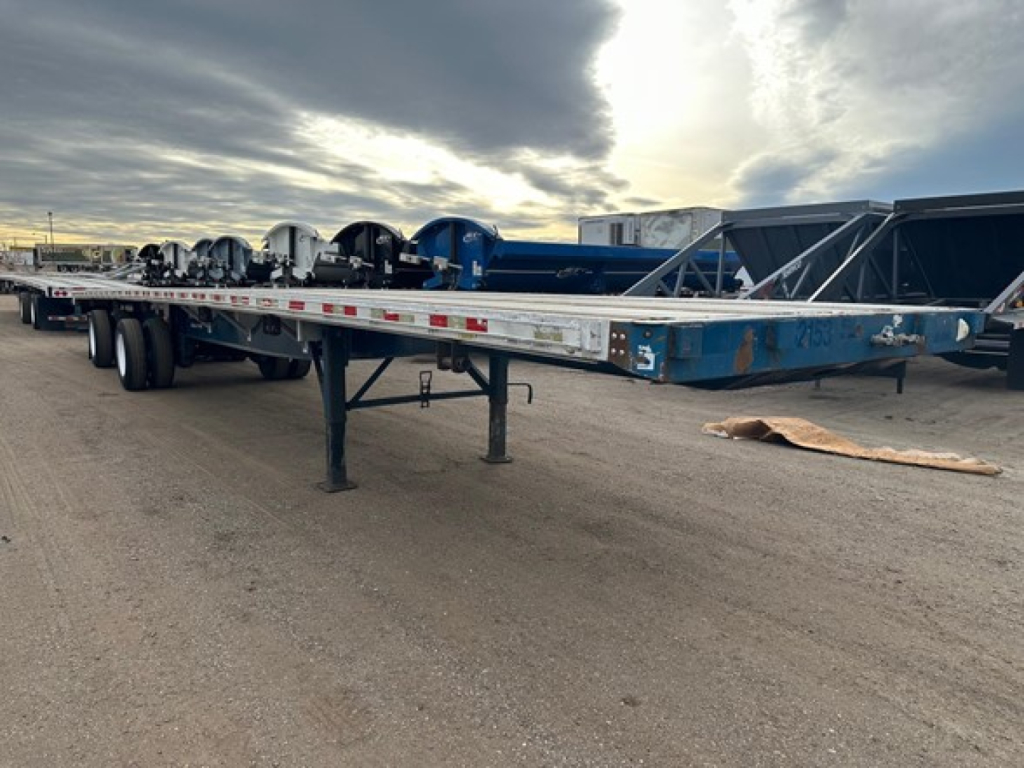 Flatbed trailer in a yard with other trailers in background, 2014 Great Dane Freedom LT listing.