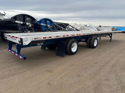 Flatbed trailer with dual rear axles and white frame, viewed from side, carrying equipment and coil rollers.