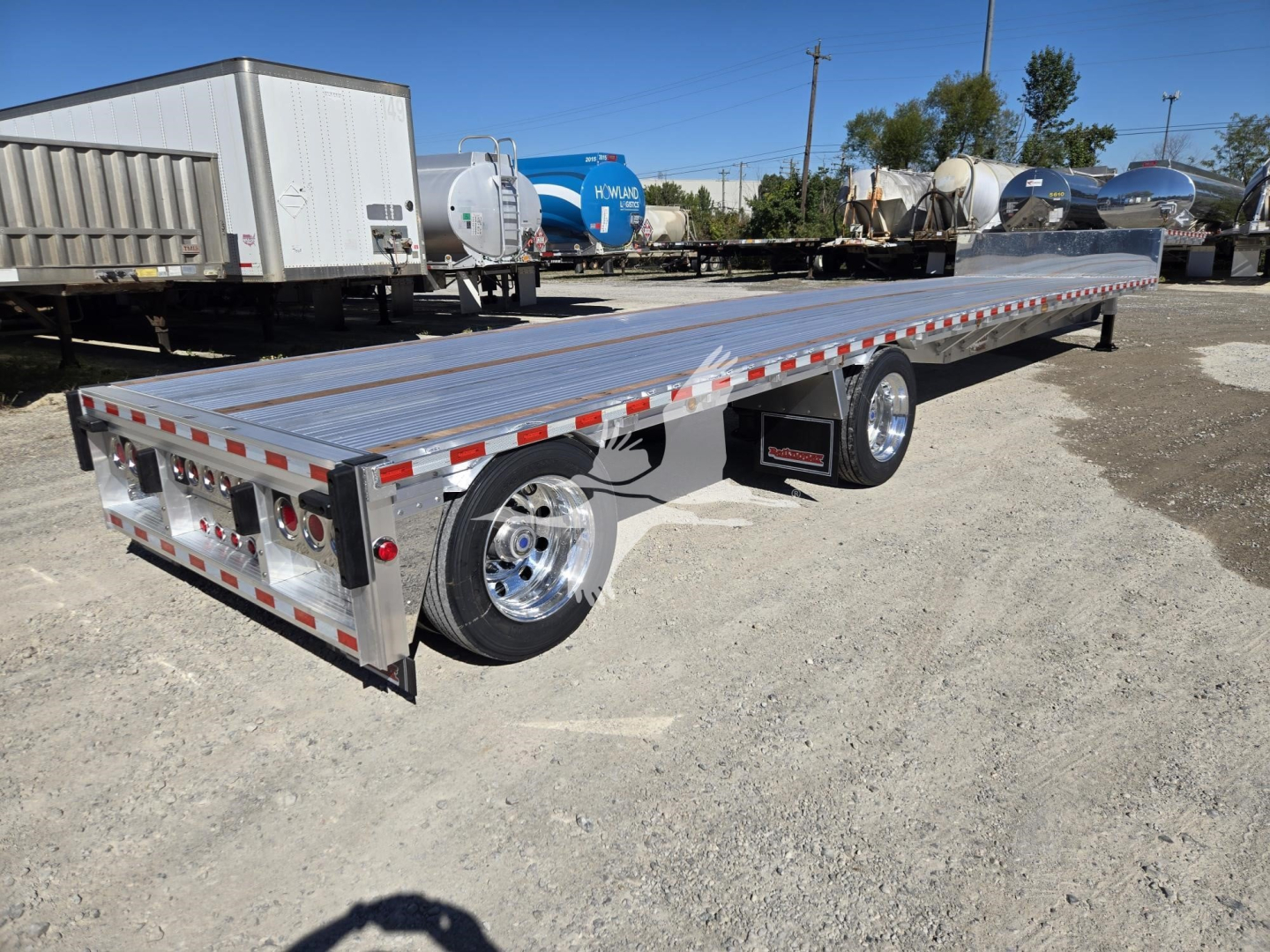 Trailer showing a long flatbed dropdeck with dual rear axles, aluminum deck, reflective tape, and chrome wheels.
