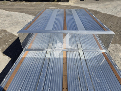 Trailer deck showing Reitnouer Big Bubba dropdeck with metal corral/brace and grooved aluminum surface; visible riveted joints and wood stringers along the deck.