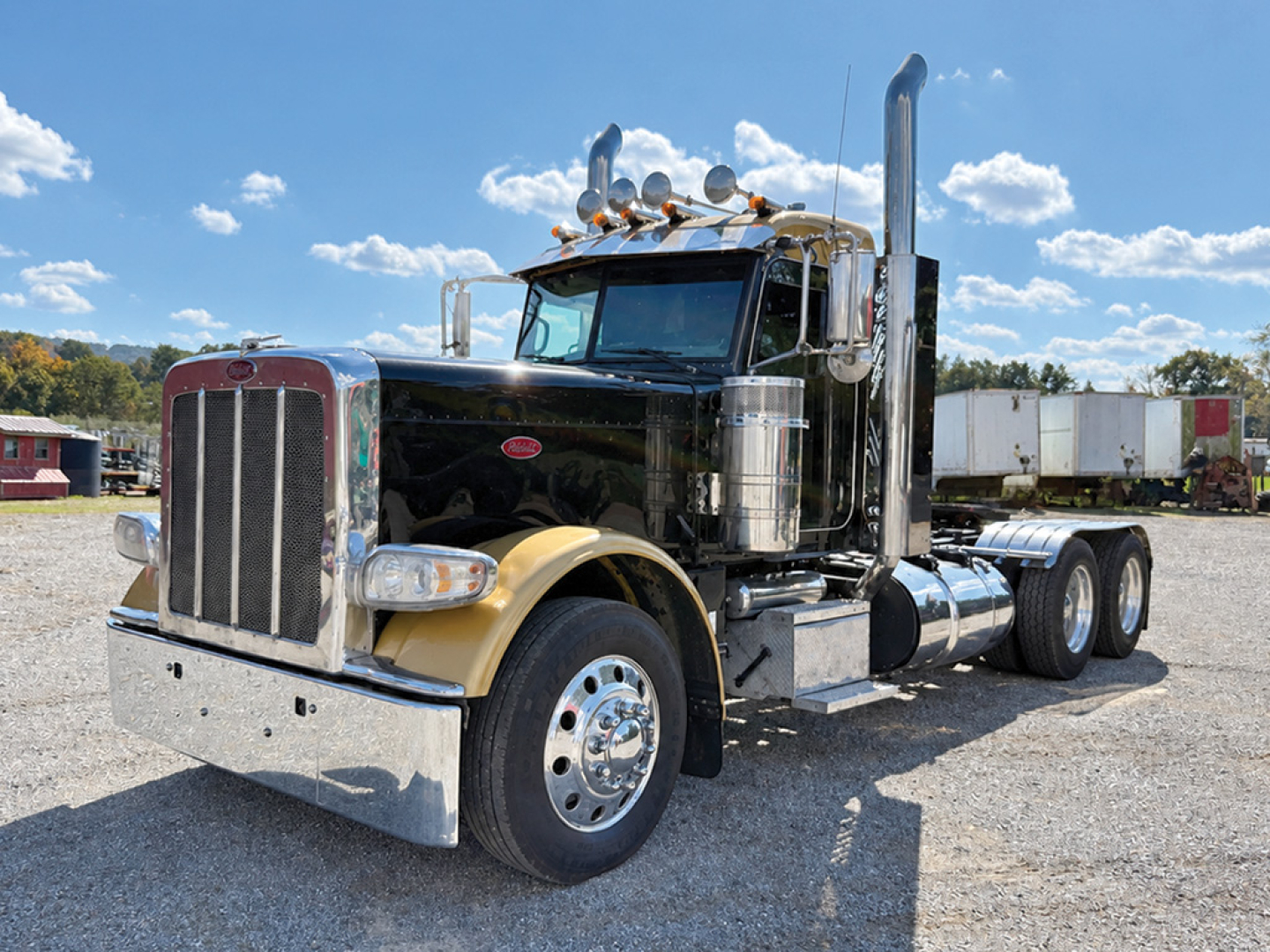Peterbilt 389 Extended Hood Fatboy truck in black and beige colors, front grille, dual exhaust stacks, chrome bumper, daycab configuration, gravel lot.