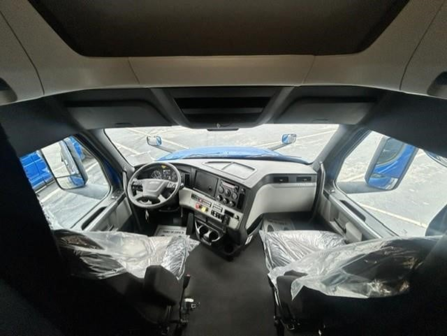 Truck cab interior of a 2022 Freightliner Cascadia 126 from the driver seat perspective, with plastic-covered seats and dashboard controls visible.