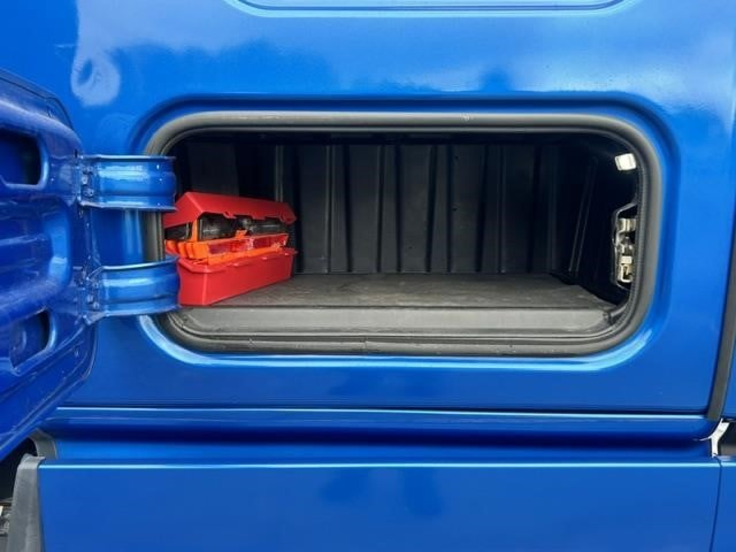 Freightliner Cascadia 126 cab storage compartment with open door showing interior, blue exterior, small red tool tray inside