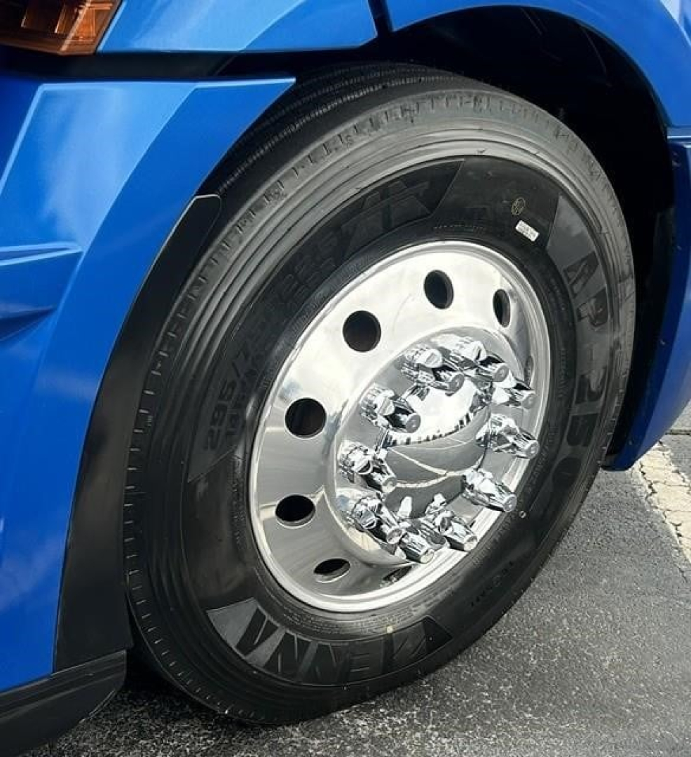 Truck wheel close-up showing steel chrome hub with lug nuts on a blue Freightliner Cascadia cab.