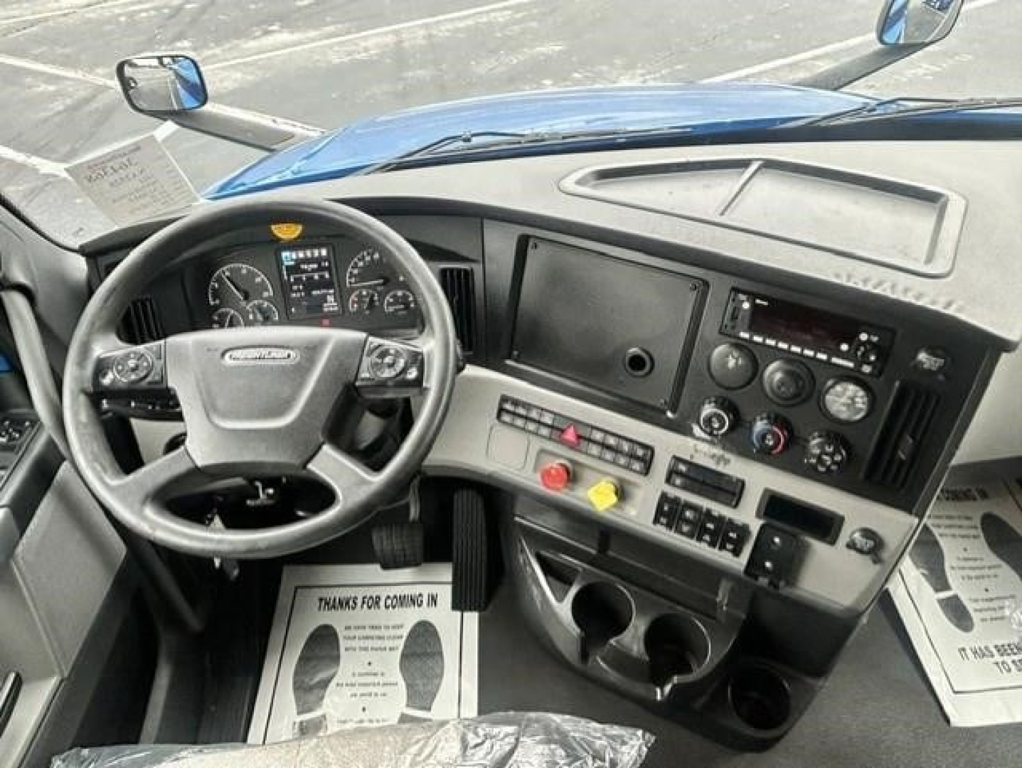 Cab interior of a Freightliner Cascadia showing steering wheel, dashboard with gauges, dual displays, and control panel.
