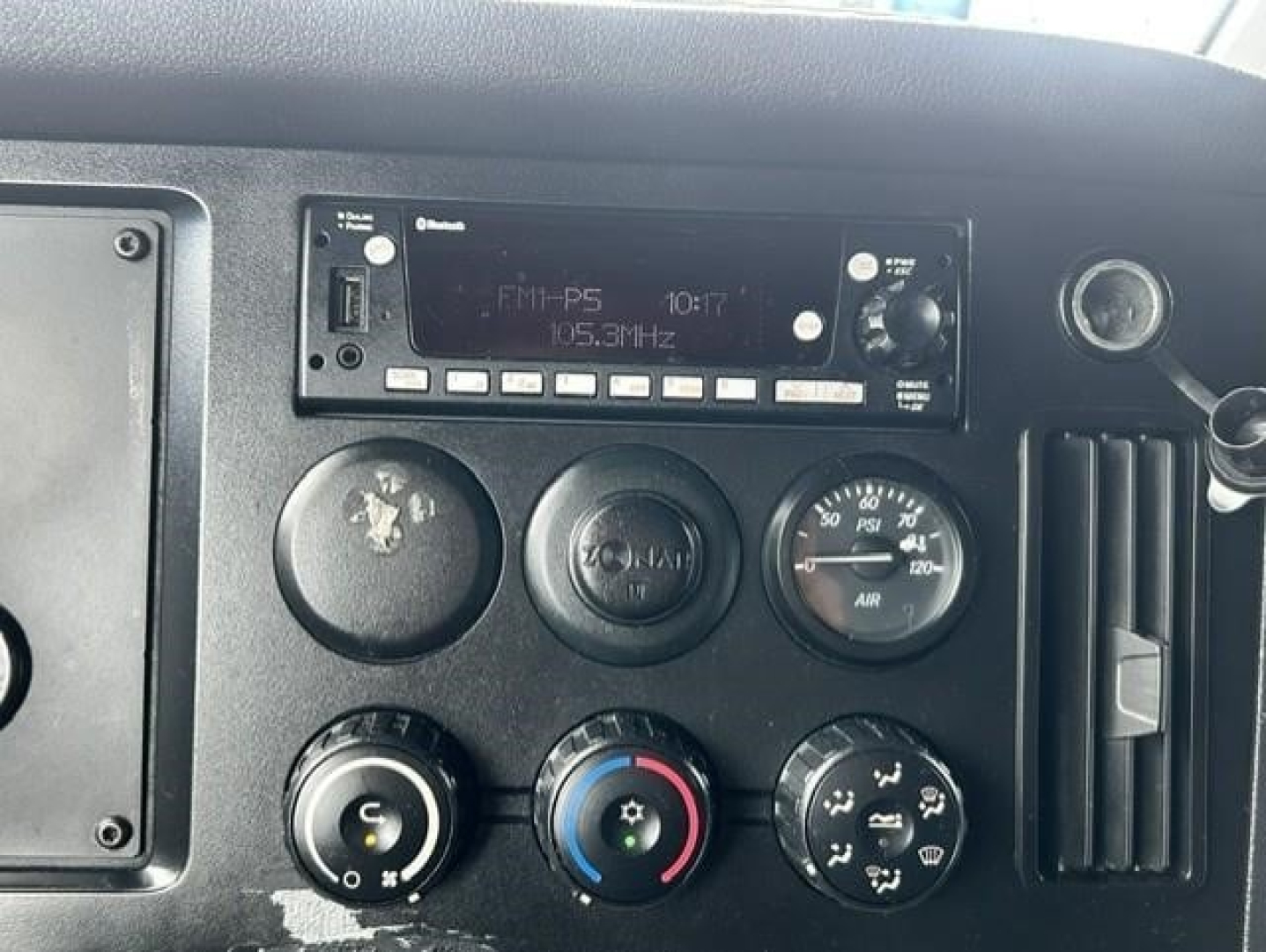 Dashboard of Freightliner Cascadia showing radio unit with FM-P5 and 105.3 MHz, climate controls with dials, and gauges.