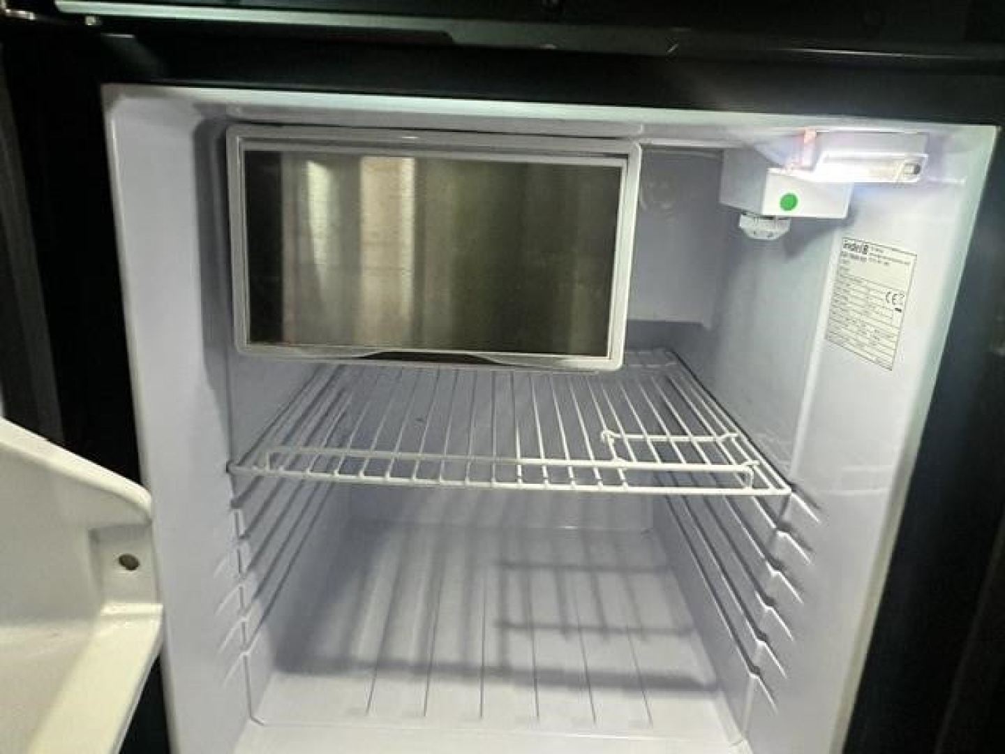 Fridge inside a Freightliner Cascadia cab showing empty freezer and refrigerator compartments with shelves.