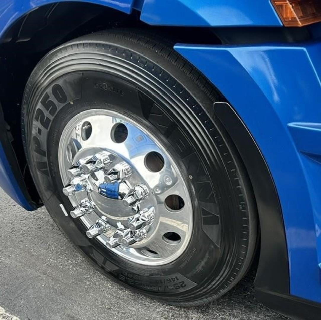 Truck wheel of a blue Freightliner Cascadia showing chrome hubcap and tire with visible branding.