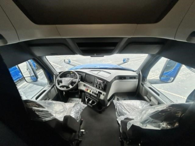 Truck cab interior of a 2022 Freightliner Cascadia 126 from the driver seat perspective, with plastic-covered seats and dashboard controls visible.