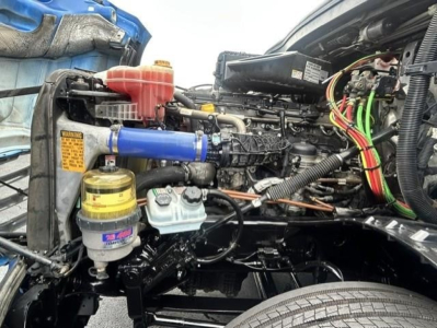 Freightliner Cascadia 126 engine bay showing blue intercooler hose, coolant reservoir, yellow oil filter cap, and various colored wiring harnesses.