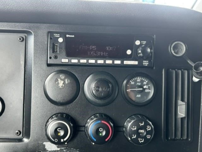 Dashboard of Freightliner Cascadia showing radio unit with FM-P5 and 105.3 MHz, climate controls with dials, and gauges.